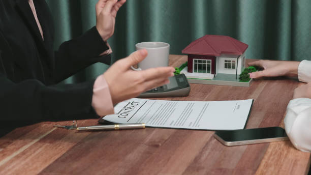 Two people discussing a real estate contract at a table with a model house.