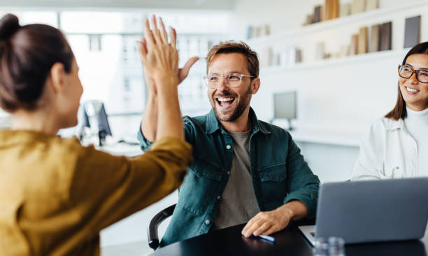 Three colleagues celebrate with a high-five at a desk in an office.