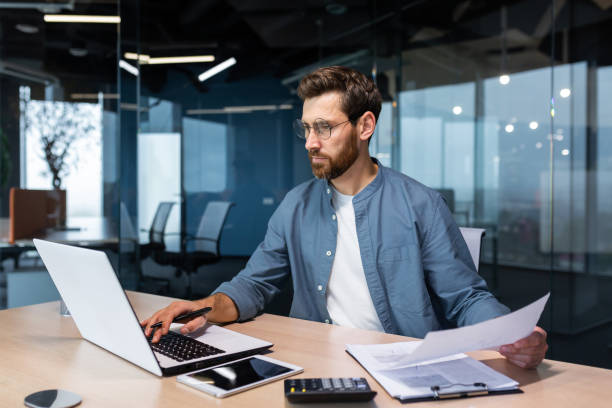 A professional reviewing documents and using a laptop at a modern office, indicative of real estate investment tasks.