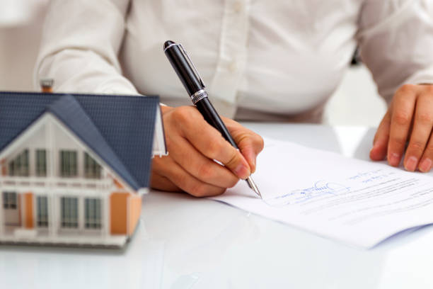 A person signs a document next to a model of a house.