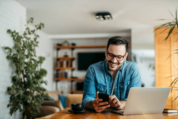 Smiling man in a modern home office researching real estate investment opportunities in Dubai on his phone.